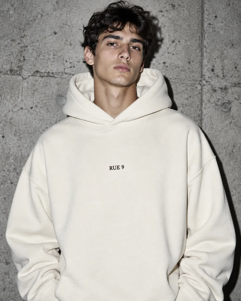 Lookbook streetwear, hoodie crème devant un mur en béton